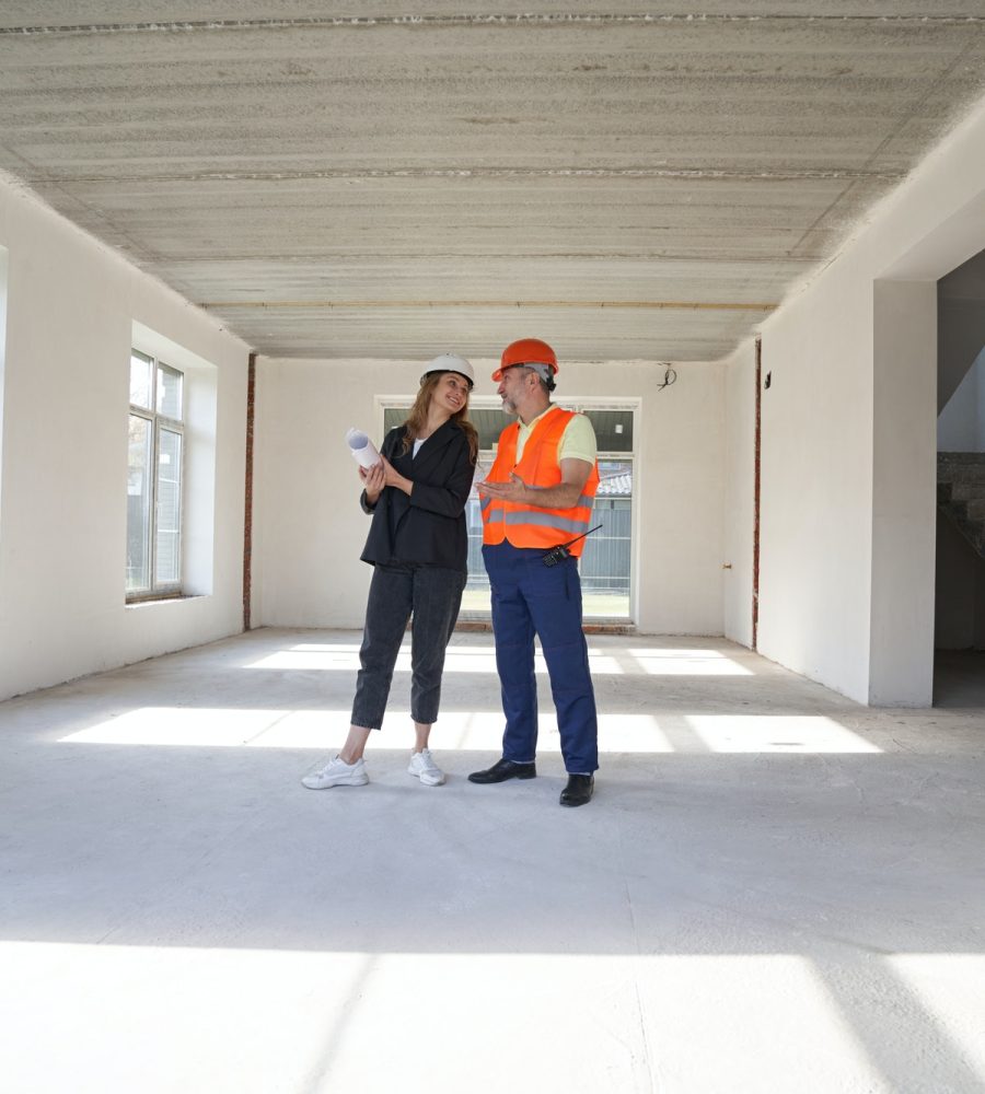 Woman engineer talking with construction worker inside house